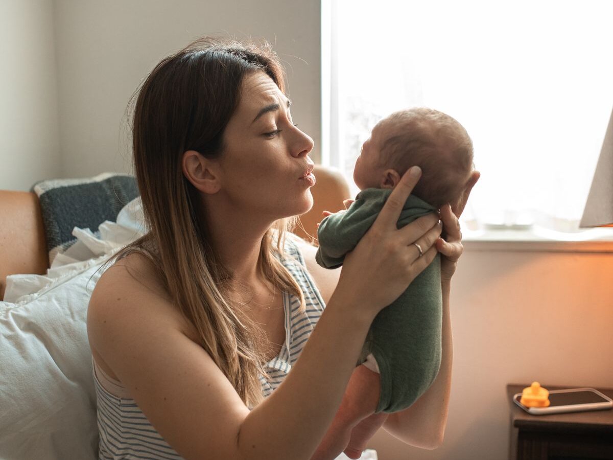 A new mother holding her baby by a bright window at home