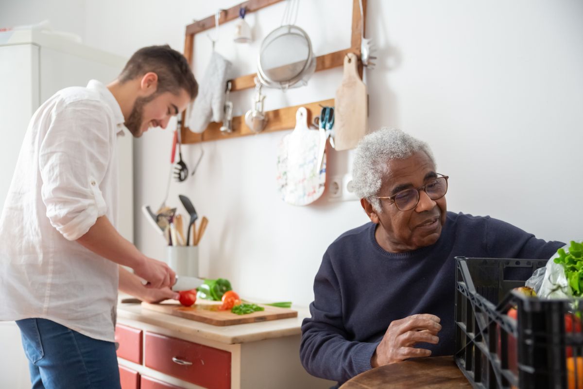 A young support worker preparing a meal with an older adult in a home kitchen