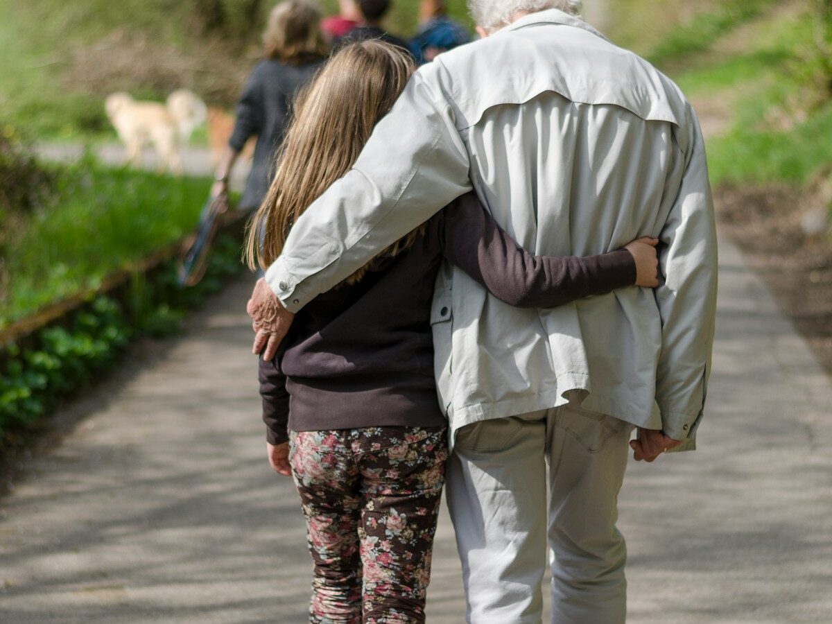 An adult walking arm in arm with an older parent outdoors